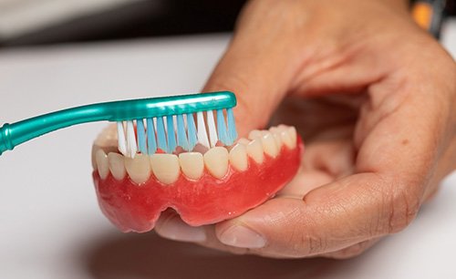 Using a toothbrush to clean dentures held in left hand