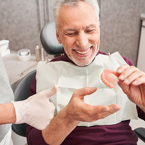 Person holding full denture under water faucet