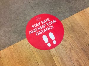 red sticker on floor that reads, “stay safe and keep your distance”