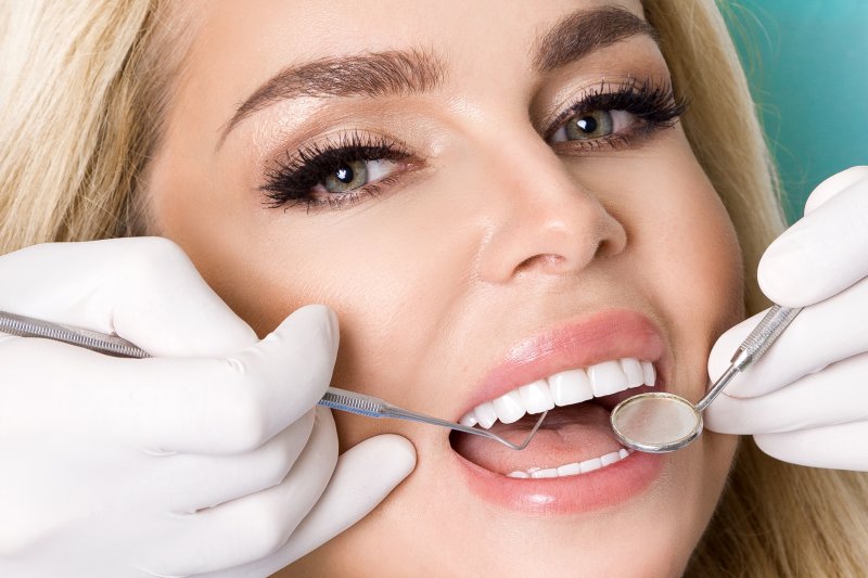 woman smiling while dentist inspects her porcelain veneers