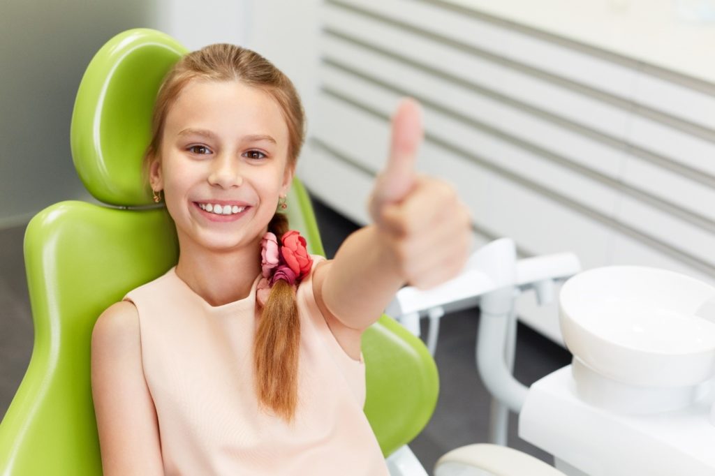 success 
Alt Image Tag: child at dentist’s office giving thumbs up
