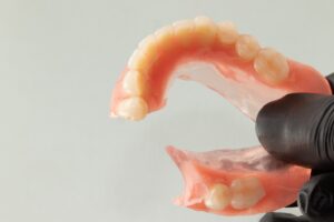 Gloved hand holding lower denture.