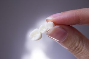 Finger and thumb holding a dental bridge